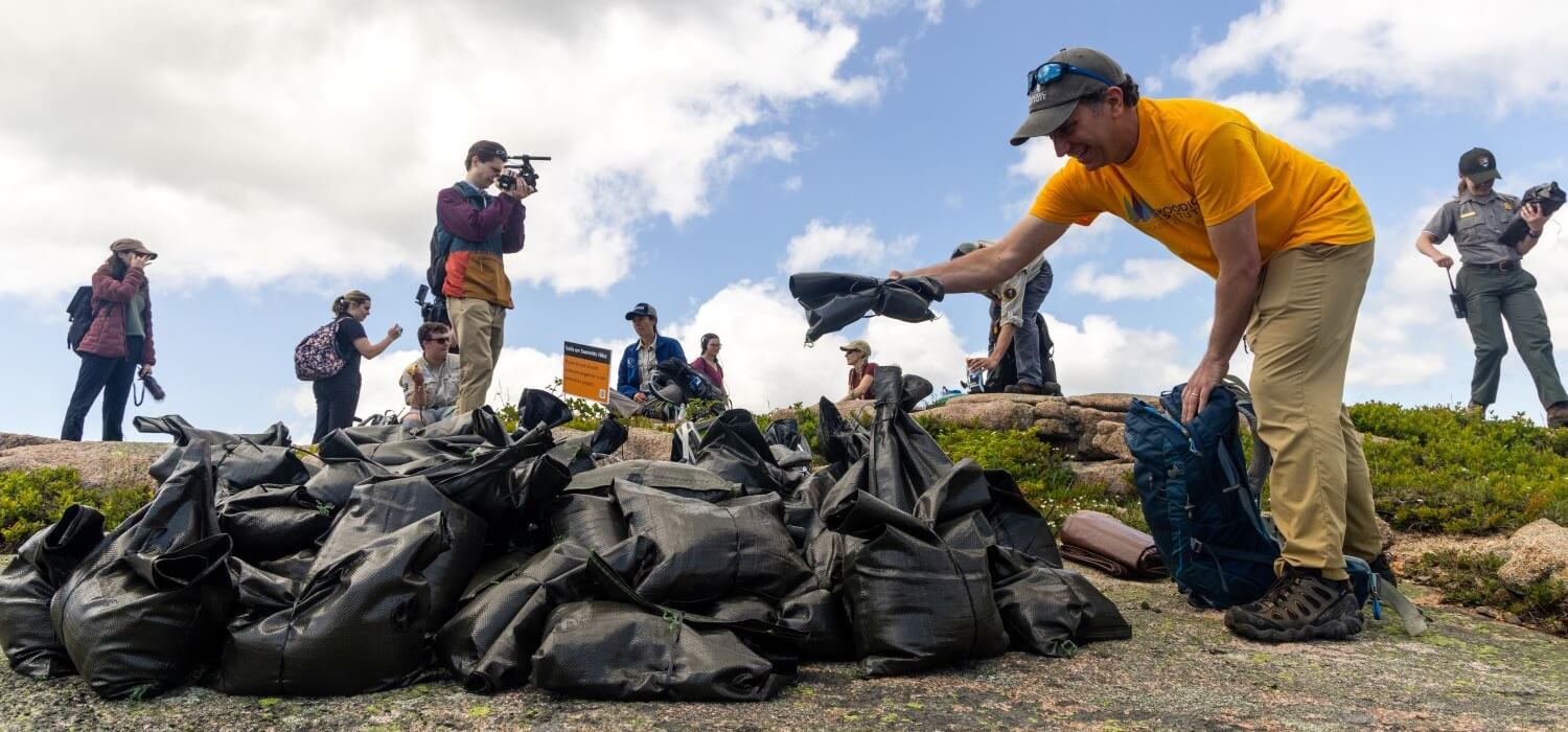 A climate adaptation scientist at the Schoodic Institute drops off a bag of soil at the summit of Sargent Mountain during the Save our Summits hike. (Photo by Sam Mallon/Friends of Acadia)